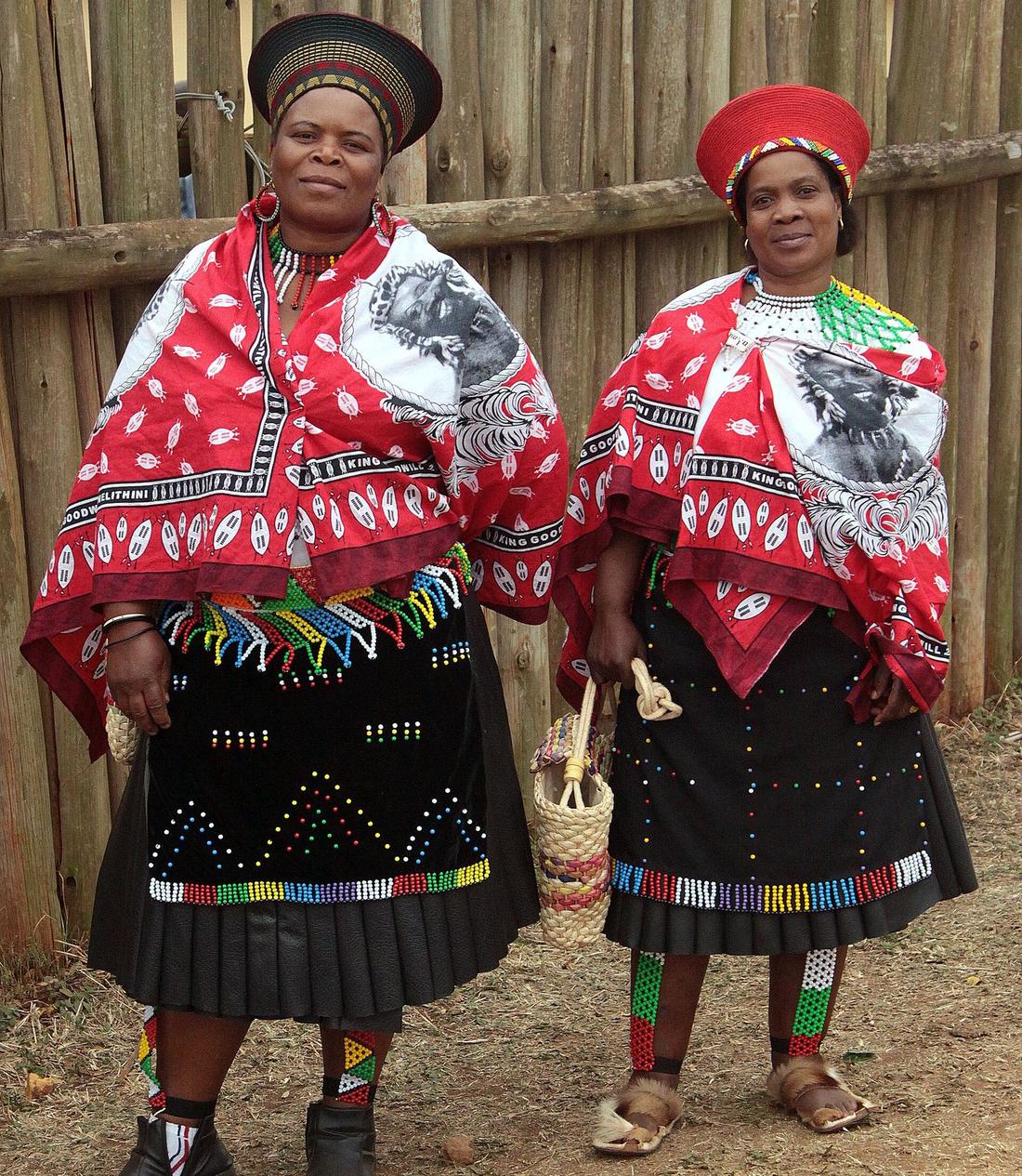 Two women in traditional Zulu dress with beaded skirts and red capes